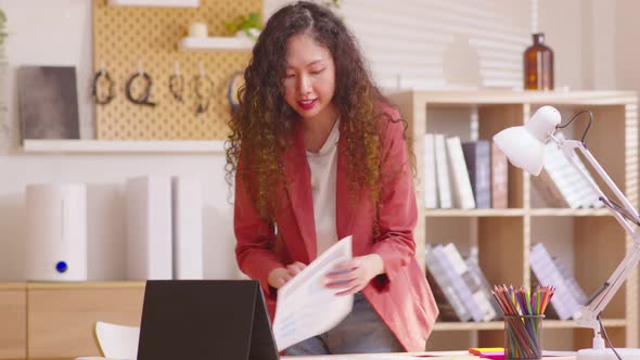 Business woman standing in front of laptop in home office showing paper sheet to customer have graph