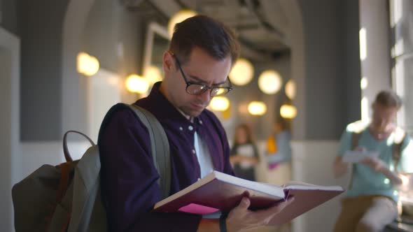 Young Student Reading Book While Standing By at Corridor in University