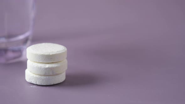 Effervescent Soluble Tablet Pills and Glass of Water on Purple Background