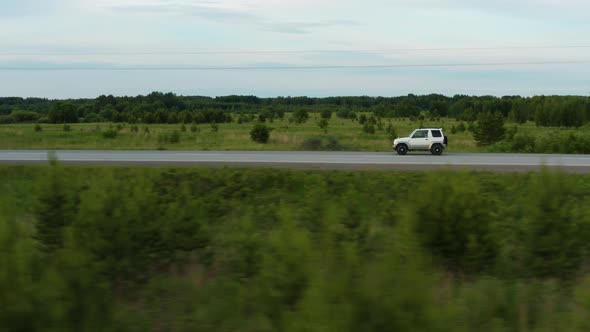 Aerial View of a Car Driving Along the Road Among Fields of Green Grass