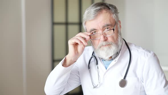 Portrait of Serious Senior Doctor Taking Off Eyeglasses Looking at Camera and Showing Covid19