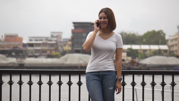 Beautiful Asian woman smiling talk to cellphone beside the river.