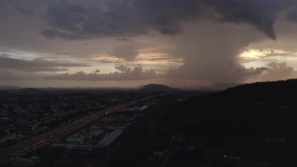 Aerial fairly stationary shot of a highway leading to a hill with heavy clouds on the horizon