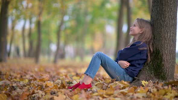 A Child Reads A Book in a Sunny Autumn Park.