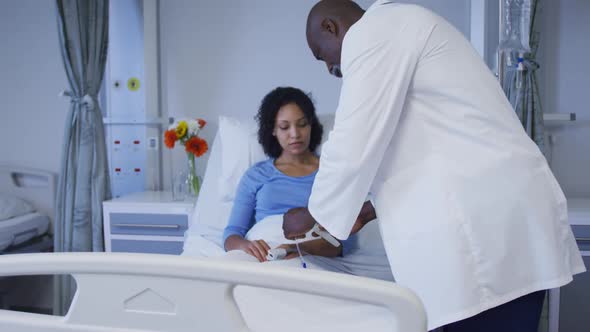 Diverse male doctor putting female patient on drip in hospital room