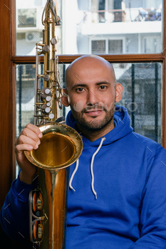 axophonist sitting on the floor at home with his saxophone looking at the camera.