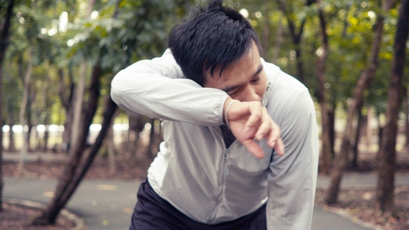 Handsome Asian man athlete runner resting exhausted after exercise training outdoors in the forest.