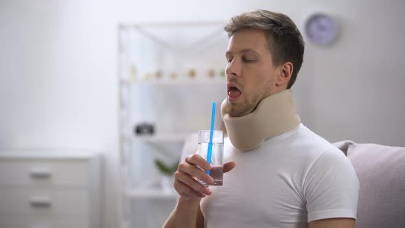 Man in Foam Cervical Collar Trying to Drink Glass Water With Straw, Poor Attempt