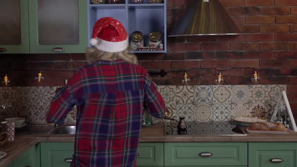 Christmas Mood Cheerful Woman Dancing in the Kitchen in a Santa Hat