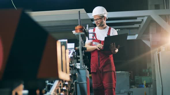 Side View of Engineer Standing with Laptop Near Rolling Mill