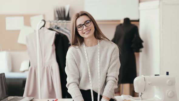 Smiling Caucasian Brunette Seamstress in the Studio Looking at the Camera and Laughing.