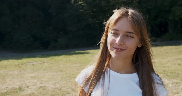 Young Attractive Female Walk and Look at the Camera with Smile on Green Lawn. Cheerfully Young Girl