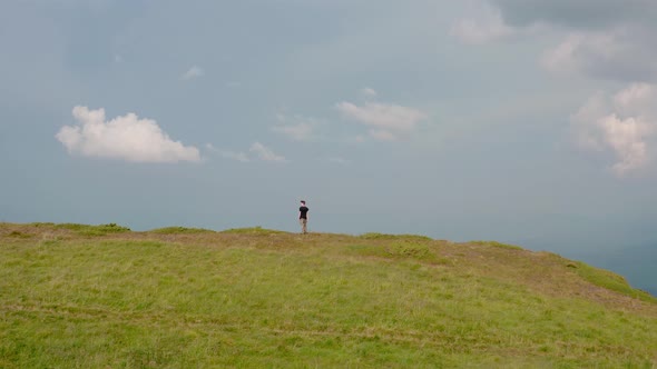 Aerial Drone View. Flying Around Young Man Standing on Top of the Mountain at Sunset