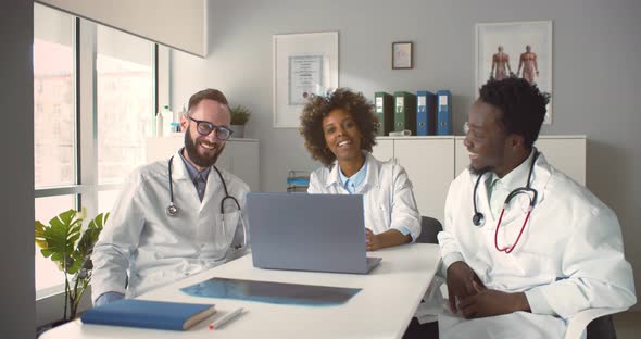 Diverse Medical Colleagues Sitting at Desk Chatting and Laughing in Clinic Office