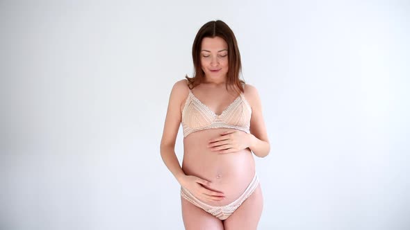 Pregnant woman in underwear on a white background posing and smiling
