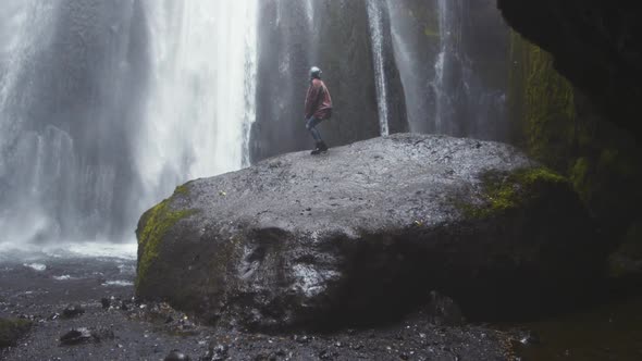 Woman Crouching On Rock To View Waterfall