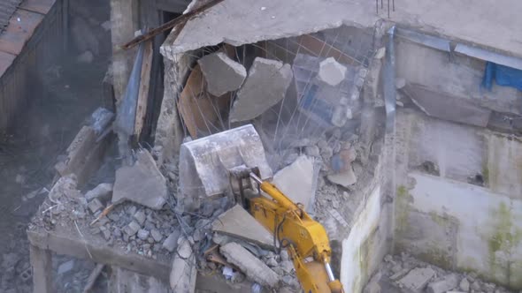 Destroying Old Concrete House Using Mechanical Arm of Bulldozer on Construction Site alt