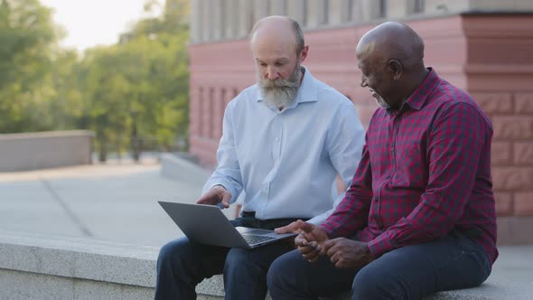 Two Elderly People Sitting Outdoors Using Laptop for Work