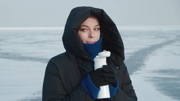 Young Woman in Warm Down Jacket with a Hood in Cold Winter on Snowy Arctic Background