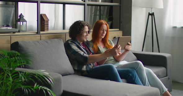 Couple Sitting on Sofa, Enjoying Video Chat with Friends on Tablet Computer