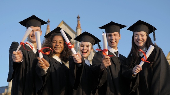 Smiling graduates posing in single line with diplomas.