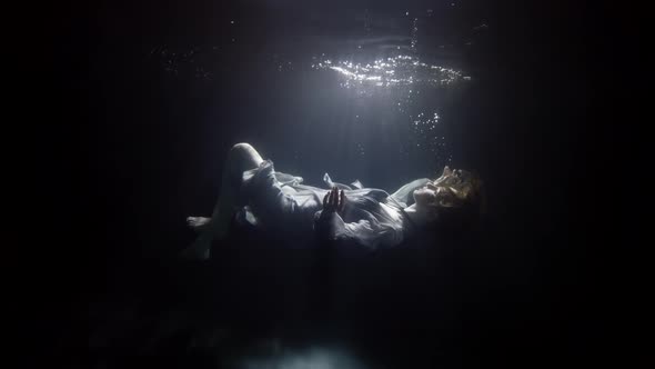 Silhouette of Sinking Woman Underwater Floating and Diving Under Surface of Dark Pool