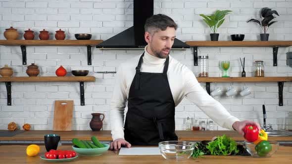 Man chef cook in home kitchen greets tells shows ingredients for cooking salad