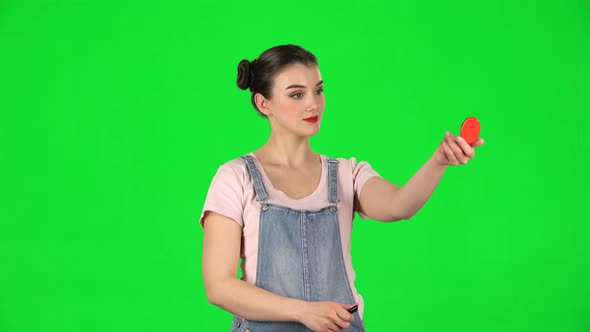 Woman with Two Hair-buns Paints Her Lips Looking in a Red Mirror on a Green Screen