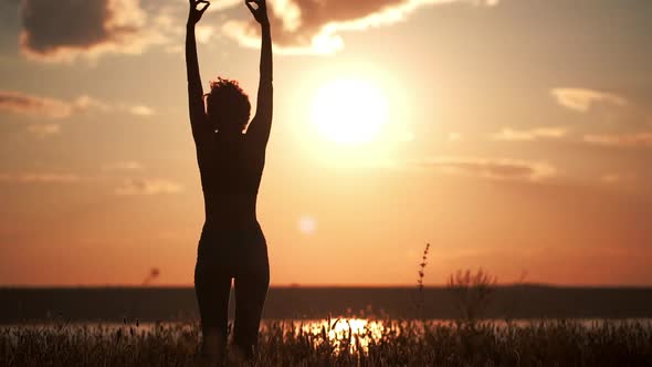 Silhouette of Young Beautiful Girl Practicing Yoga at Sunset