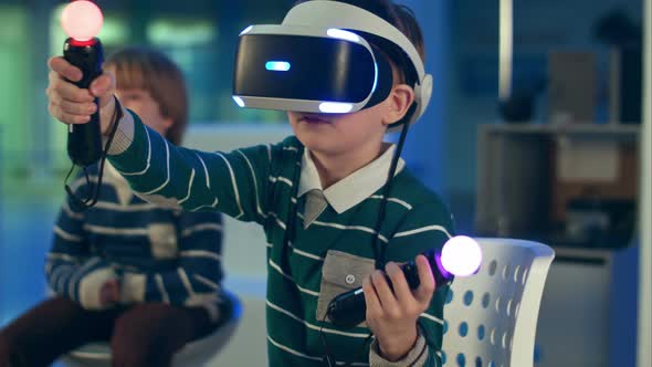 Little Boy in Vr Headset Playing Virtual Reality Game with Controllers While Another Boy Waiting