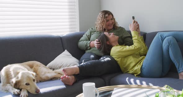 Caucasian lesbian couple smiling and sitting on couch with dog