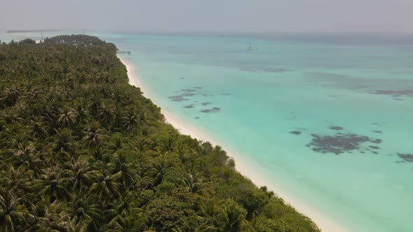 Drone flying over the Maldivian coast with many green trees against a stormy sky