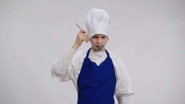 Portrait of Caucasian Little Chef Imitating Smelling Tasting Disgusting Soup From Scoop