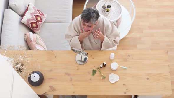 Elderly woman in bathrobe applying facial cream