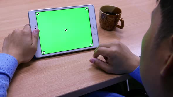Man is using tablet with green screen on the wooden table