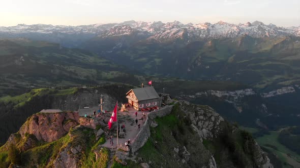 Early morning drone view to Swiss mountain top with mountain restaurant and first guests. Swiss flag