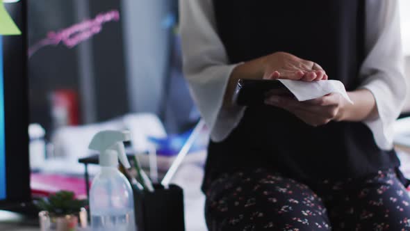 Mid section of woman cleaning digital tablet with tissue at modern office