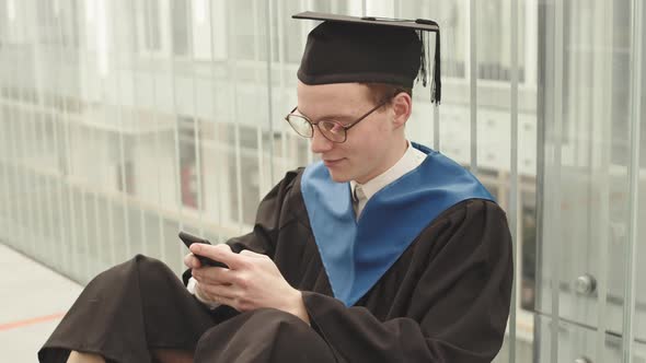 Caucasian Male Graduate Typing Message on Telephone