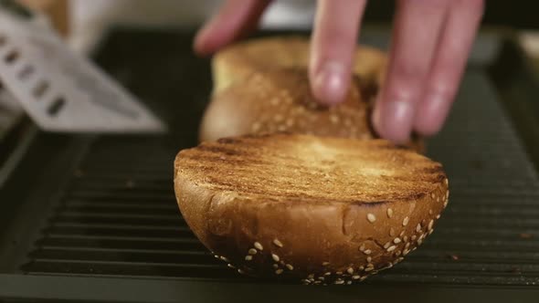 Professional male chef roasts and turns sliced buns on hot grill pan.