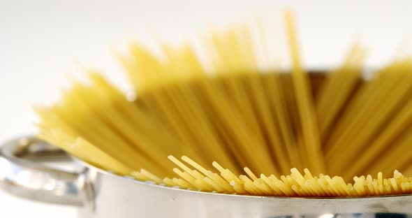 Raw spaghetti arranged in silver container ready to be cooked on white background