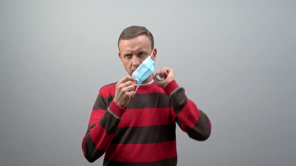 Man Wearing a Grey Shirt Putting on a Mask on a White Background