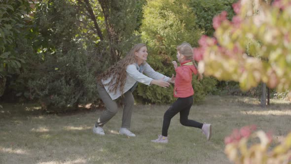 Little Caucasian Girl in Red Jacket Running To Her Beautiful Smiling Mother in the Park. Woman with