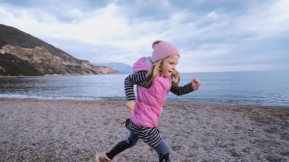 Cute little girl in pink hat runs along the beach along the sea in spring time. Freedom concept