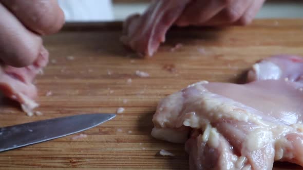 Person Cutting Raw Chicken Meat In A Wooden Board At The Kitchen - close up shot