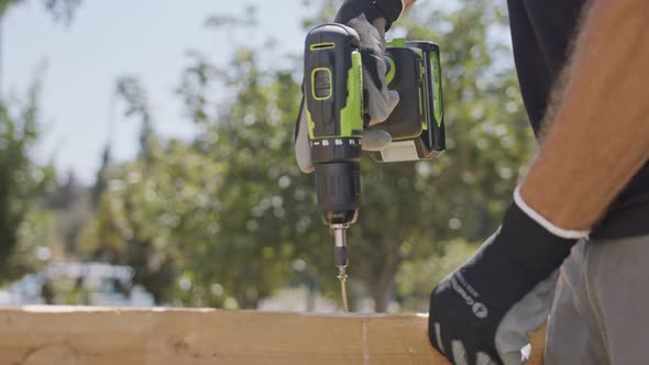 Slow motion of a man using an electric screwdriver to drive a screw into wood