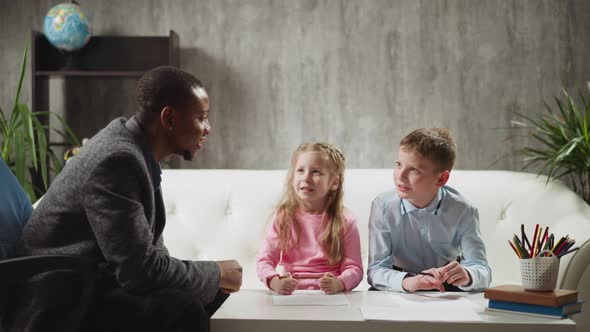 Little Girl Answers Nodding Tutor and Classmate Sits on Sofa