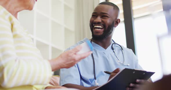 Video of happy african american male doctor giving medicines to caucasian senior woman