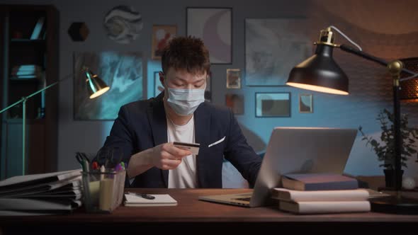 Portrait of Young Asian Man Wearing Medical Mask Doing Shopping on Laptop Computer Using Bank Credit