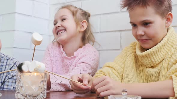 Two Teenage Girls and a Boy Fry Marshmallows By Putting Them on Sticks and Holding Candles Over the