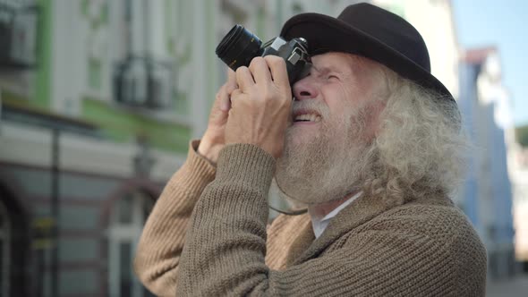 Close-up of Positive Senior Tourist Taking Photo of Sight in European City and Smiling at Camera